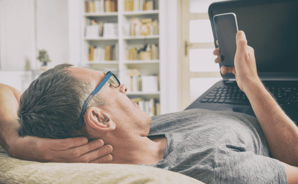 man with hearing aid rests head back on hand while looking at smartphone
